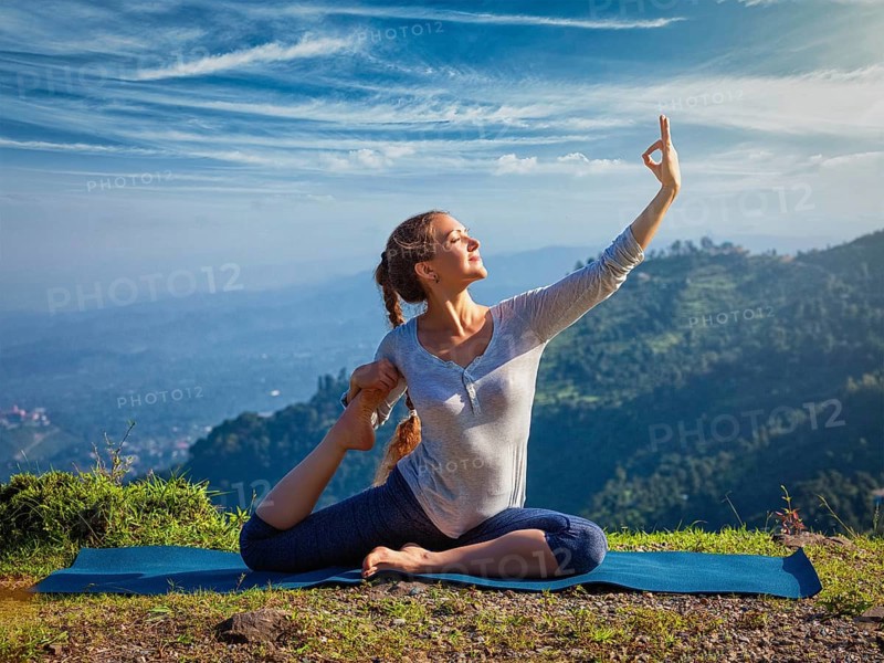 Yoga outdoors, young sporty fit woman doing stretching yoga asana Eka pada rajakapotasana, one-legged king pigeon pose in Himalayas mountains, India, Asia