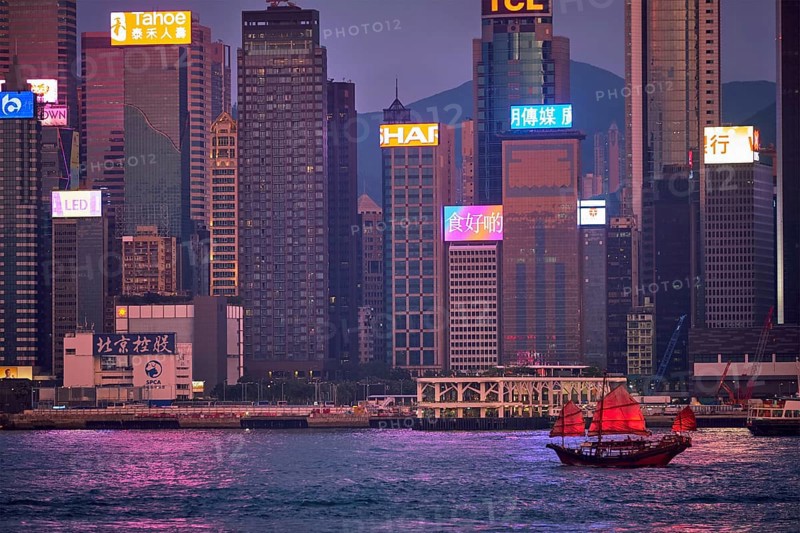 HONG KONG, CHINA, MAY 1, 2018: Tourist junk boat ferry with red sails and Hong Kong skyline cityscape downtown skyscrapers over Victoria Harbour in the evening. Hong Kong, China, Asia
