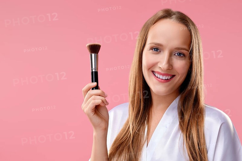 Beautiful girl with makeup brush in hand over pink background