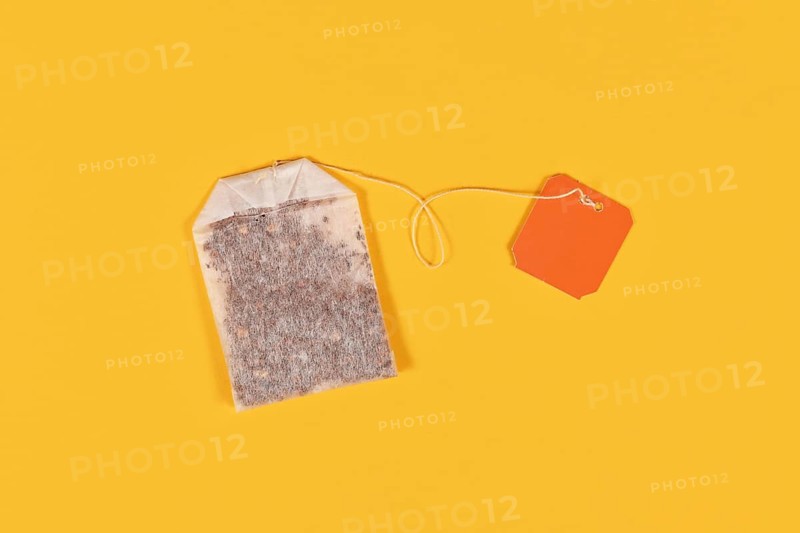 Tea bag with blank orange label on yellow background