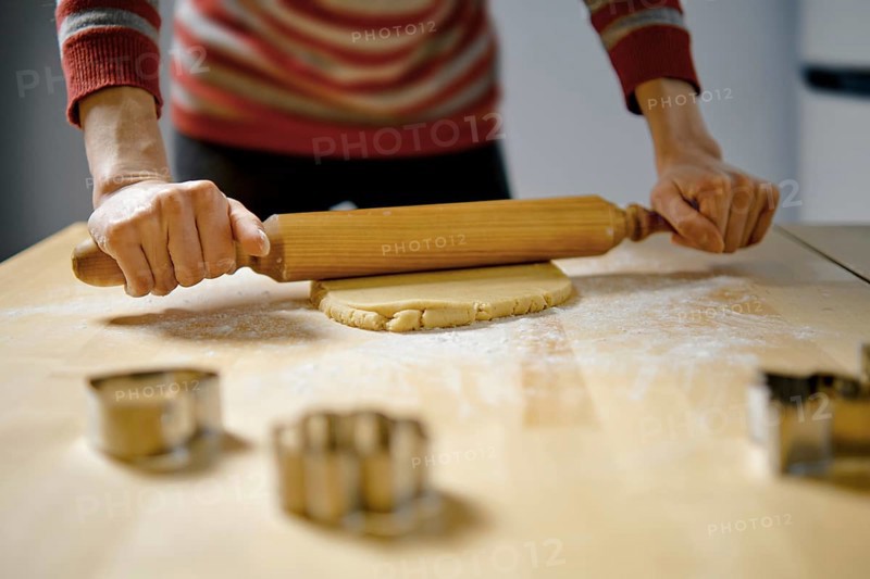 Unrecognizable woman rolls out ginger dough with rolling pin on kitchen table (low angle view with selective focus photo)