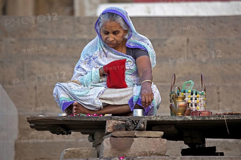 Old Indian woman sitting on ghat and praying near the Ganges river at Varanasi, Uttar Pradesh, India, Asia