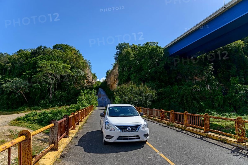 Car parked in the sun on one of the two bridges over the Chavon River surrounded by lush vegetation, Altos de Chavon, La Romana, Dominican Republic, Hispaniola, Caribbean, Central America