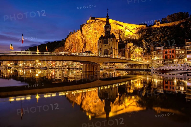 Night view of Dinant town, Collegiate Church of Notre Dame de Dinant over River Meuse and Pont Charles de Gaulle bridge and Dinant Citadel illuminated in the evening. Dinant, Belgium, Europe