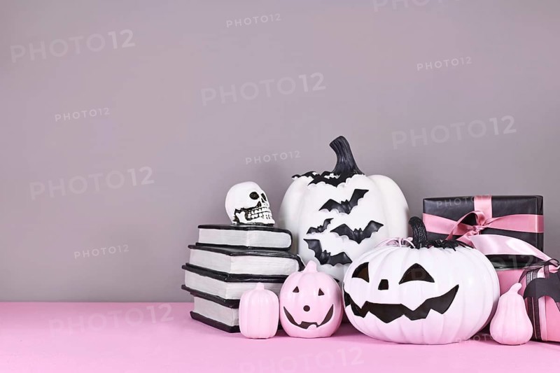 Pink and white Halloween decor with black and white pumpkins, spell books and spiders on gray background with copy space