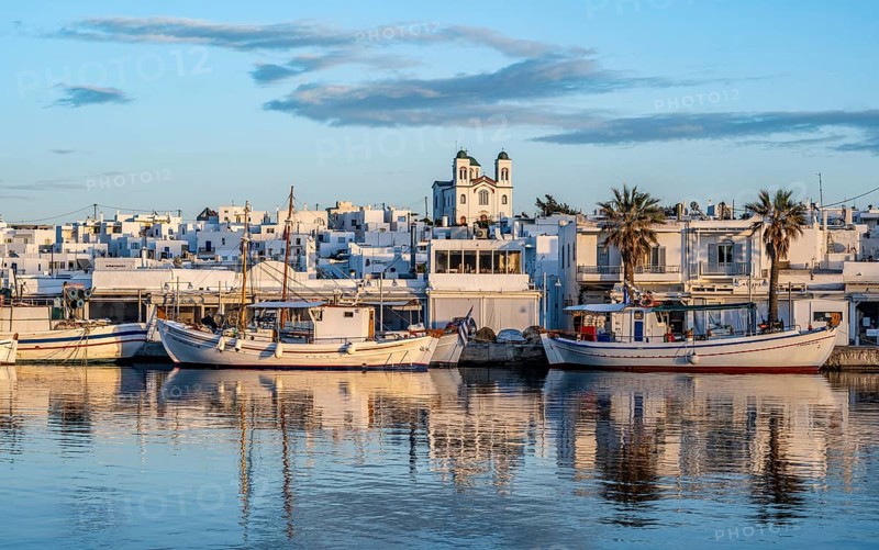 View of Naoussa, Fishing boats in the harbour at sunset, reflected in the sea, White Cycladic houses and church Agios Faneromeni, Naoussa, Paros, Cyclades, Greece, Europe