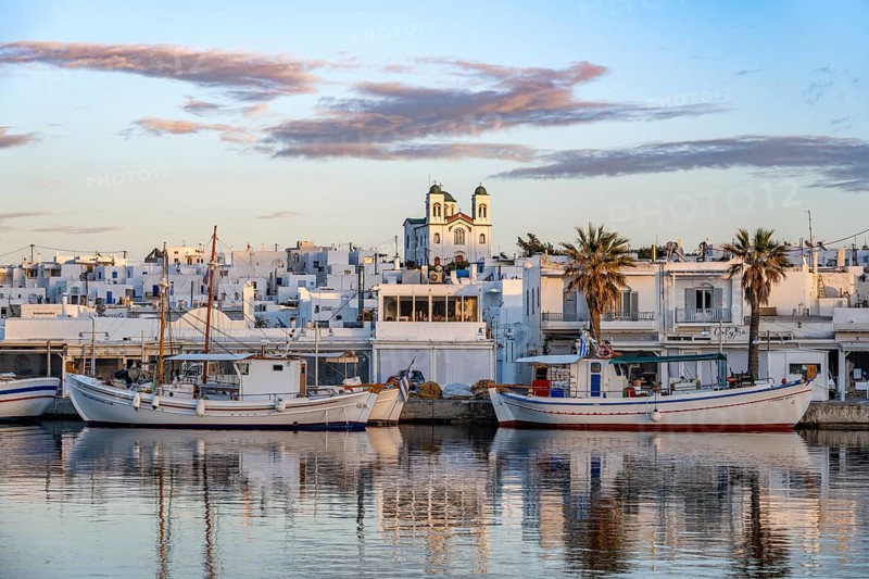View of Naoussa, Fishing boats in the harbour at sunset, reflected in the sea, White Cycladic houses and church Agios Faneromeni, Naoussa, Paros, Cyclades, Greece, Europe