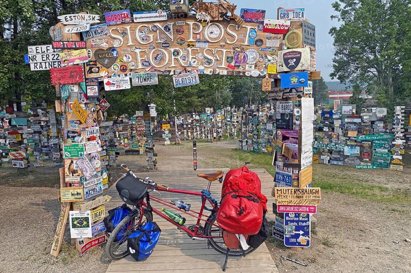 Bicycle with luggage in front of town and road signs in the signpost forest, cycling trip, cycling adventure, Watson Lake, Yukon Territory, Alaska Highway, Canada, North America