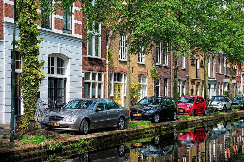 Delft, Netherlands, May 12, 2017: Cars and bicycles parked on canal embankment in street of Delft with reflection. Delft, Netherlands