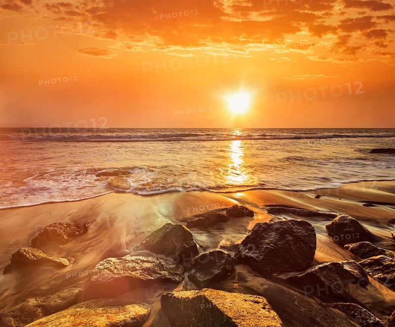Tropical beach vacation background, waves and rocks on beach on sunset with beautiful cloudscape. With lens flare and light leak