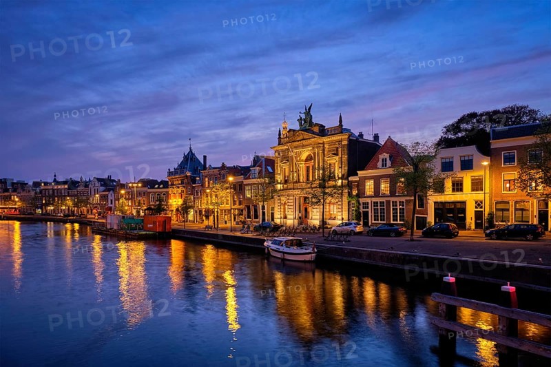 Spaarne river with boats and houses including Tylers museum illuminated in the evening. Haarlem, Netherlands