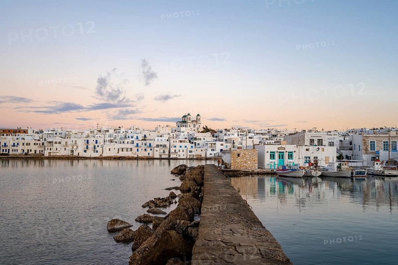 Harbour wall, view of the town of Naoussa and blue sea, at sunset, harbour with fishing boats and reflection, white Cycladic houses and church of Agios Faneromeni, Paros, Cyclades, Greece, Europe