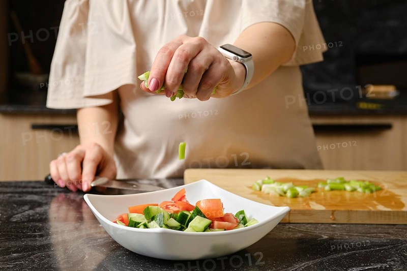 Closeup of hand of woman dropping a sliced celery stalk into a dish with salad