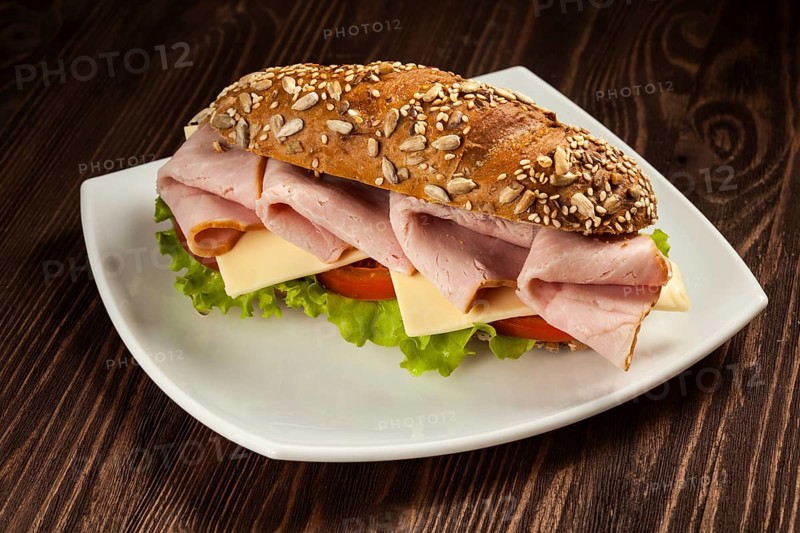 Ham sandwich with lettuce, cheese, tomato on plate on wooden table