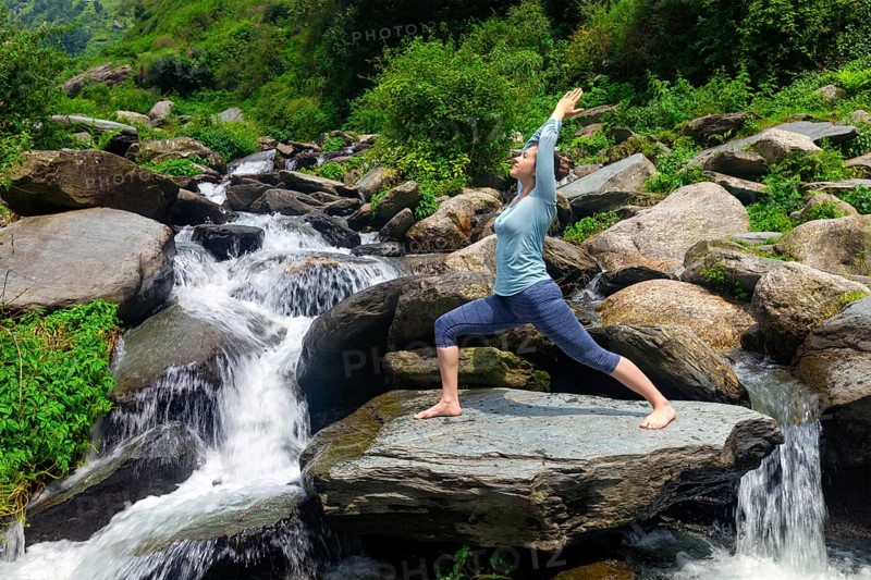 Yoga outdoors, sporty fit woman doing Ashtanga Vinyasa Yoga asana Virabhadrasana 1 Warrior pose posture at waterfall in HImalayas mountains