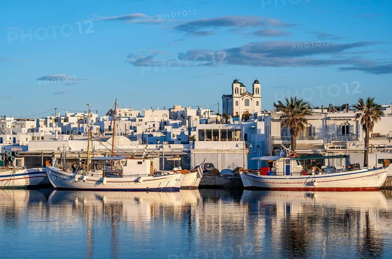 View of Naoussa, Fishing boats in the harbour at sunset, reflected in the sea, White Cycladic houses and church Agios Faneromeni, Naoussa, Paros, Cyclades, Greece, Europe