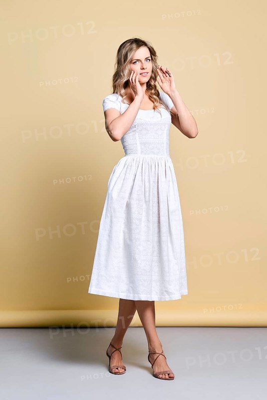 Beautiful young woman in white sundress lifting hands to fix her curly hair