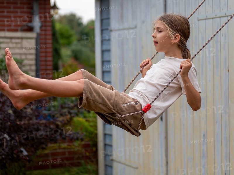 Boy swinging while sitting on children's swing at shed and garden gate, Germany, Europe