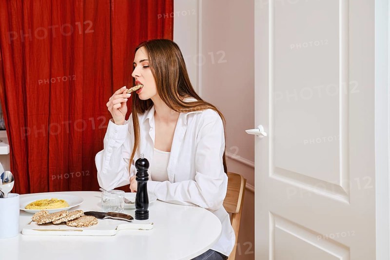 Young woman biting piece of buckwheat cracker with homemade hummus