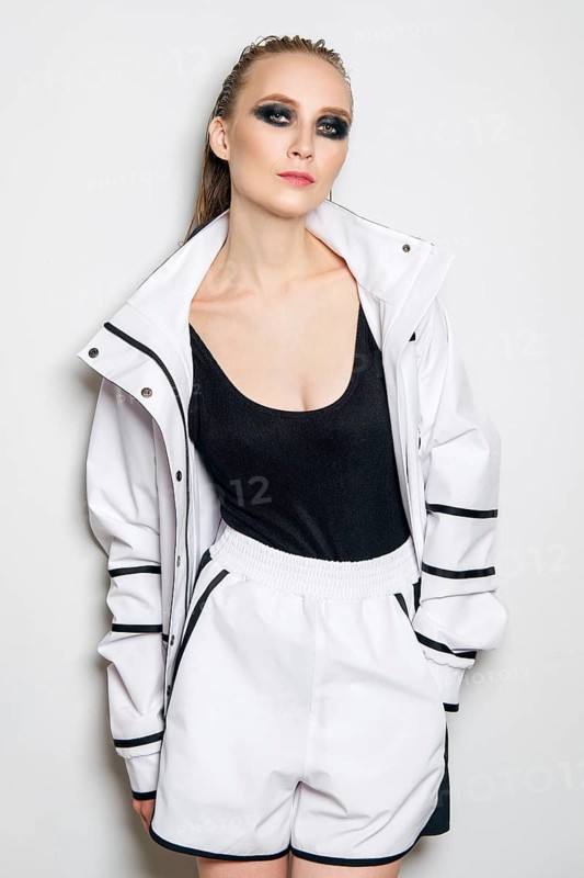 Portrait of fashion model in white sports suit. Girl in unzipped jacket, sleeveless t-shirt and wide shorts, sportive outfit
