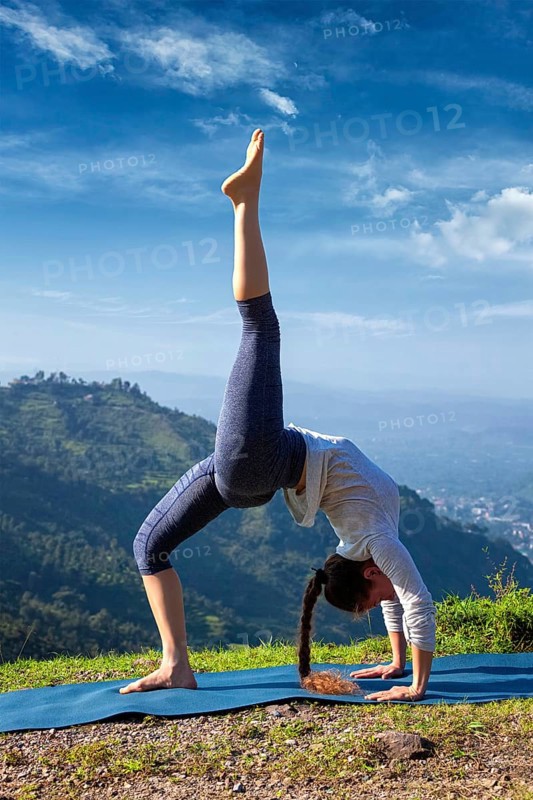 Yoga outdooors, woman doing yoga asana eka pada urdva dhanurasana Upward Bow Pose back bend outdoors in Himalayas in the morning