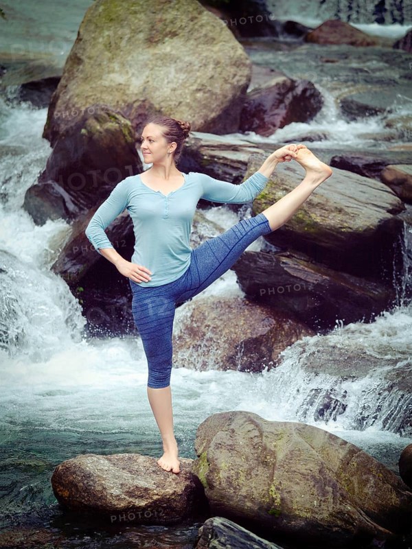 Yoga outdoors, woman doing Ashtanga Vinyasa Yoga balance asana Utthita Hasta Padangushthasana, Extended Hand-To-Big-Toe Pose position posture outdoors at waterfall. Vintage retro hipster style image