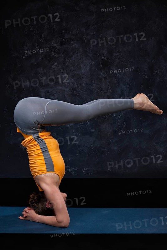 Woman doing Hatha yoga Ashtanga Vinyasa Yoga asana sirsasana, headstand variation Urdhva dandasana, upward facing staff pose on dark grund background