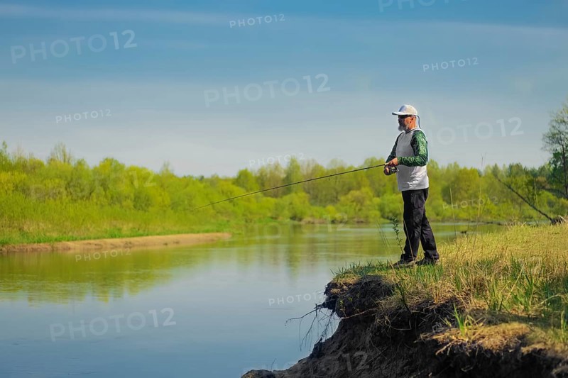 Man fish with spinning on river bank, casting lure. Outdoor weekend activity. Photo with shallow depth of field taken at wide open aperture