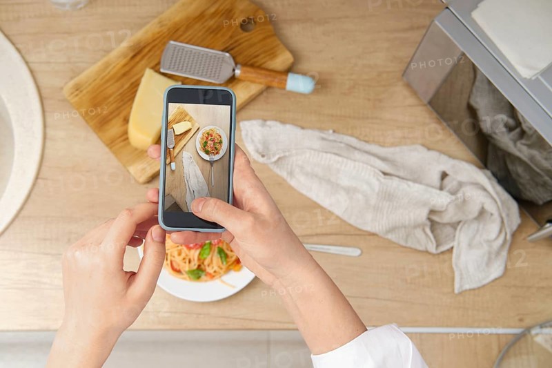 View from above of unrecognizable woman with smartphone taking photo of plate with pasta with tomato sauce for culinary blog at home. Food blogger recording video of ready spaghetti