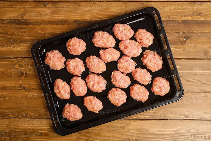 Top view of raw meatballs of minced meat on a baking tray on kitchen table
