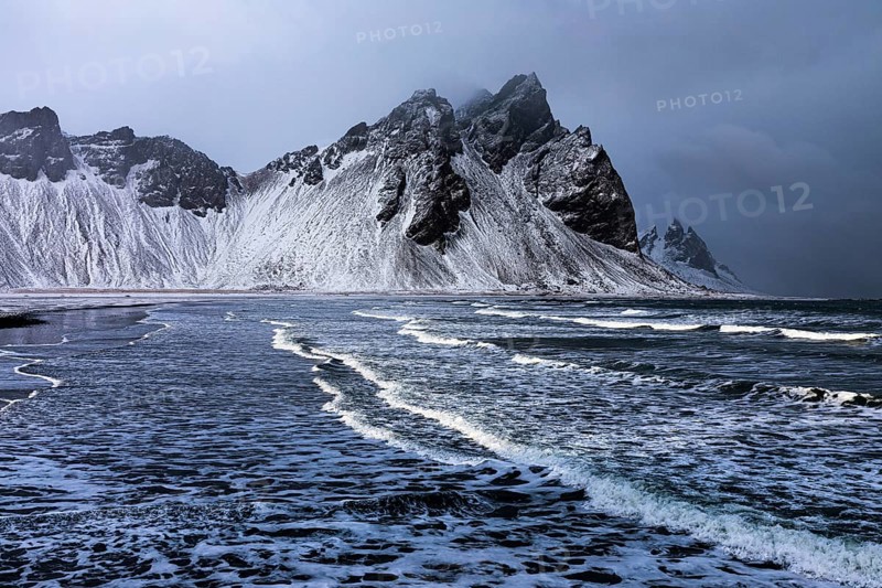 White foamy waves on the beach of Stokkness, behind snowy rocky slopes of Vestrahorn, near Höfn, Sudausturland, Iceland, Europe