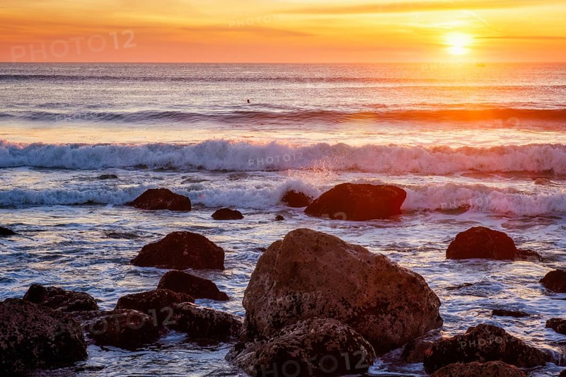 Atlantic ocean sunset with waves and rocks and surfers silhouettes in water at Costa da Caparica, Portugal, Europe