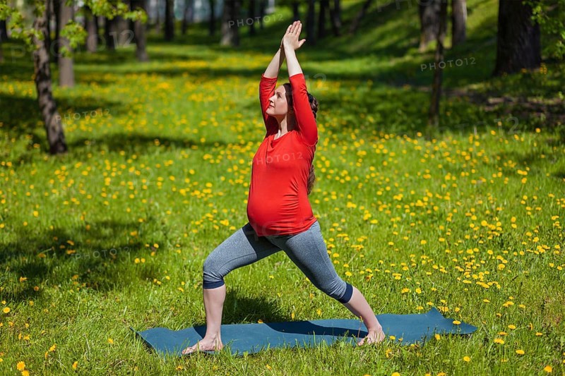 Pregnancy yoga exercise, pregnant woman doing yoga asana Virabhadrasana warrior pose outdoors on grass in summer