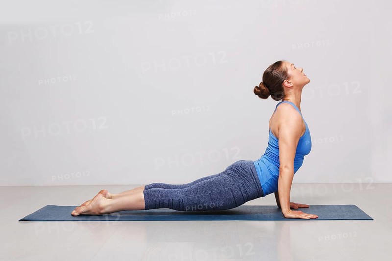 Woman doing Ashtanga Vinyasa yoga asana Urdhva mukha svanasana, upward facing dog pose on yoga mat on yoga mat in studio on grey bagckground