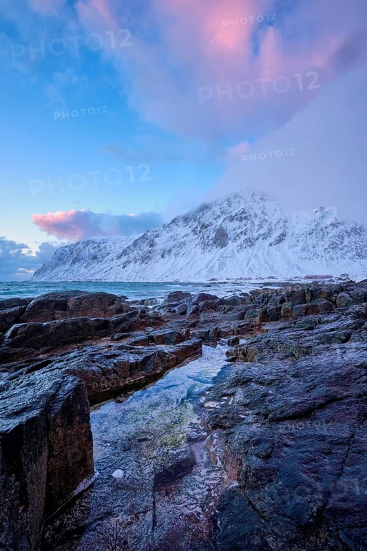Beach of Norwegian sea on rocky coast in fjord on sunset in winter. Vareid beach, Lofoten islands, Norway, Europe