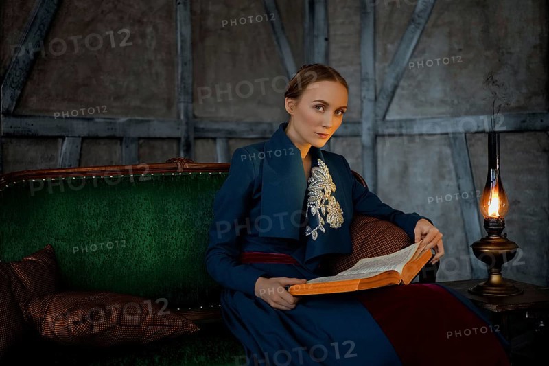 Attractive lady in oldfashioned clothes reading ancient book near vintage kerosene lamp