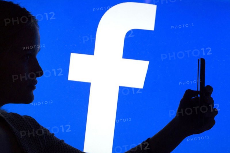 Silhouette of a woman with a smartphone in her hand in front of a Facebook logo, 12/01/2016