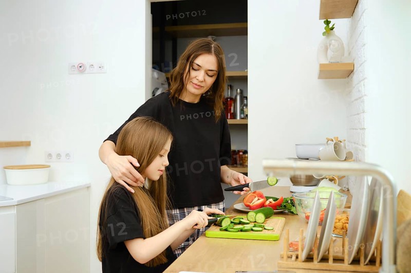 Caring mother moves her daughter's hair to the side so that it does not interfere with her cutting cucumbers