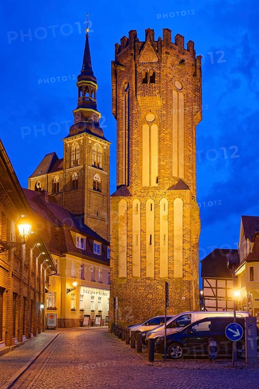 The Owl Tower at Hühnerdorfer Tor, built in brick Gothic style and illuminated at night, in the old town centre of Tangermünde. Behind it is the church of St Stephen. Tangermünde, Hanseatic town in the Altmark. Saxony-Anhalt, Germany, Europe