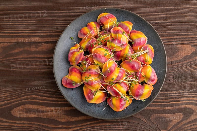 Rainbow colored dumplings with pepper, herbs, microgreen on brown wooden background. Top view, flat lay, close up