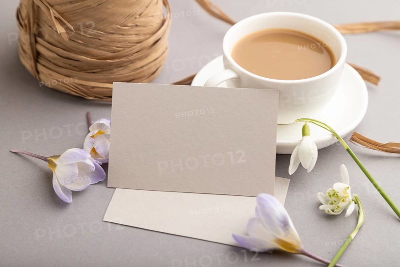 Gray paper business card mockup with spring snowdrop crocus and galanthus flowers and cup of coffee on gray background. Blank, business card, side view, copy space, still life. spring concept