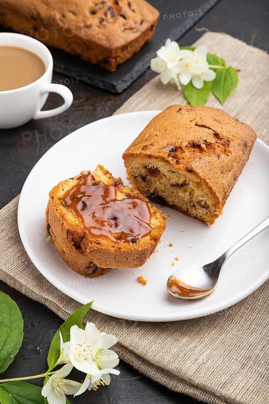 Homemade cake with raisins, almonds, soft caramel and a cup of coffee on a black concrete background and linen textile. Side view, close up