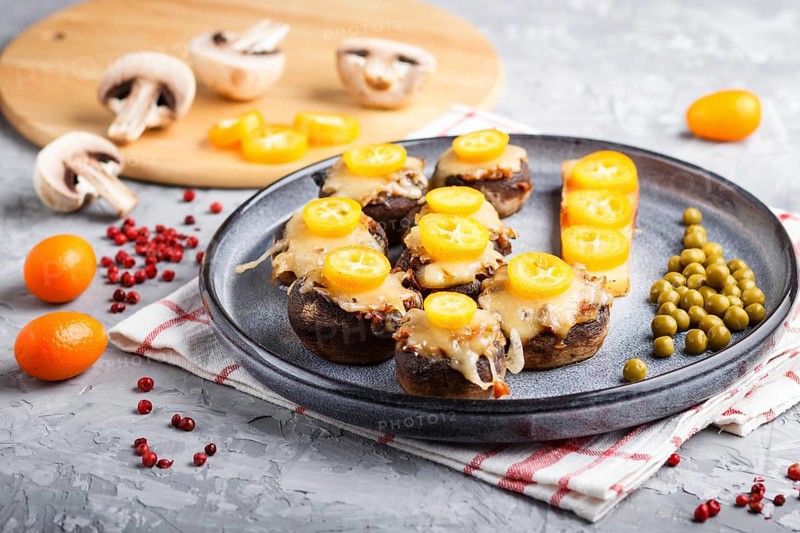 Stuffed fried champignons with cheese, kumquats and green peas on a gray concrete background. ceramic plate, side view, close up, horizontal