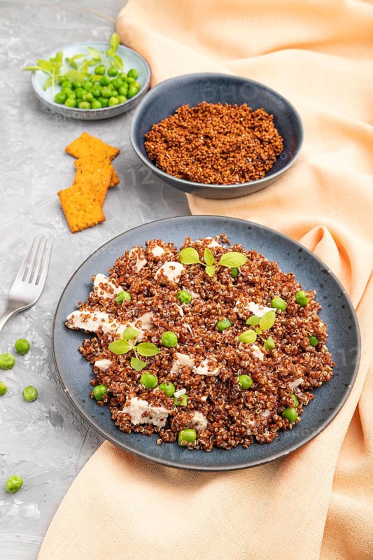 Quinoa porridge with green pea and chicken on ceramic plate on a gray concrete background and orange textile. Side view, close up