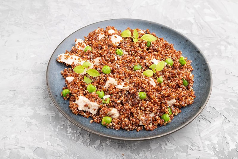 Quinoa porridge with green pea and chicken on ceramic plate on a gray concrete background. Side view, close up