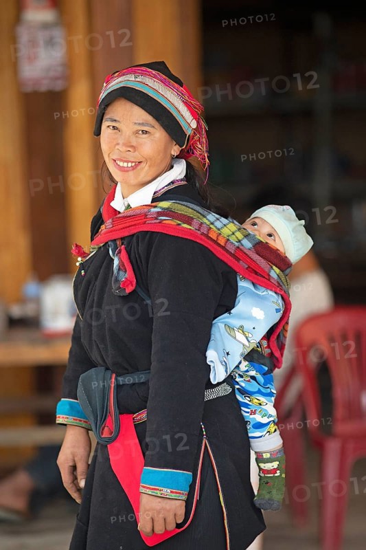 Vietnamese woman, 43 years old, in traditional traditional costume of the Dao minority, carrying her son, 3 months, on her back, Nam Dam Dao Cultural Village, Ha Giang province, Vietnam, Asia