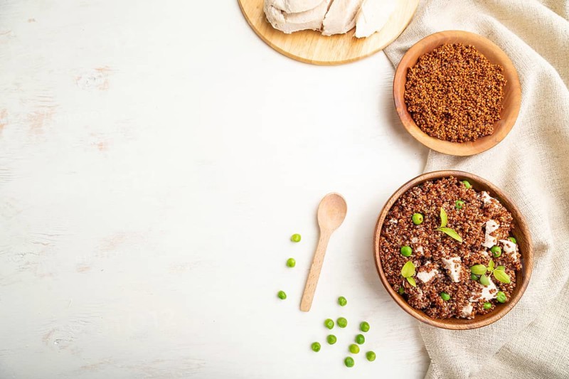 Quinoa porridge with green pea and chicken in wooden bowl on a white wooden background and linen textile. Top view, flat lay, copy space