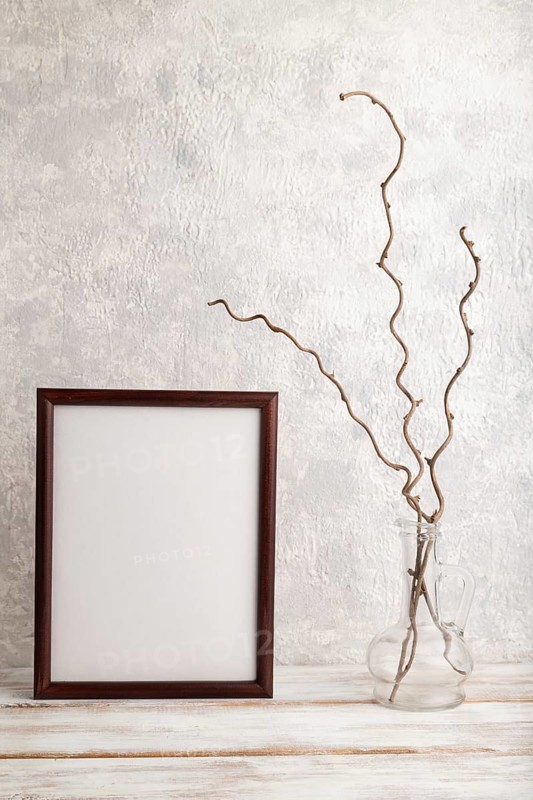 Brown wooden frame mockup with dried wine branch in glass on gray concrete background. Blank, vertical orientation, still life, copy space