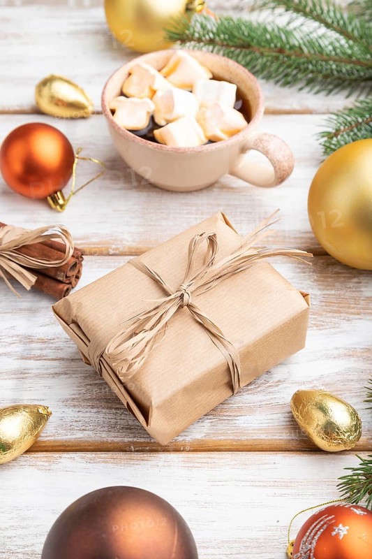 Christmas or New Year composition. Decorations, box, golden balls, cinnamon, fir and spruce branches, cup of coffee, on a white wooden background. Side view, copy space