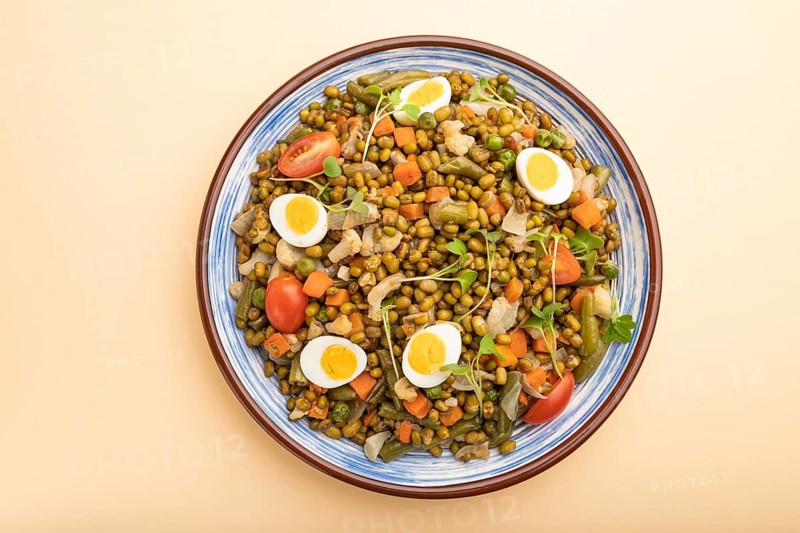 Mung bean porridge with quail eggs, tomatoes and microgreen sprouts on a pastel orange background. Top view, close up